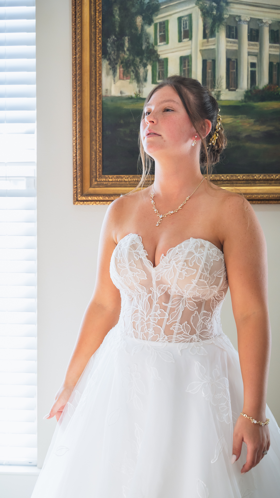 Bride in dress standing in front of a painting in bedroom
